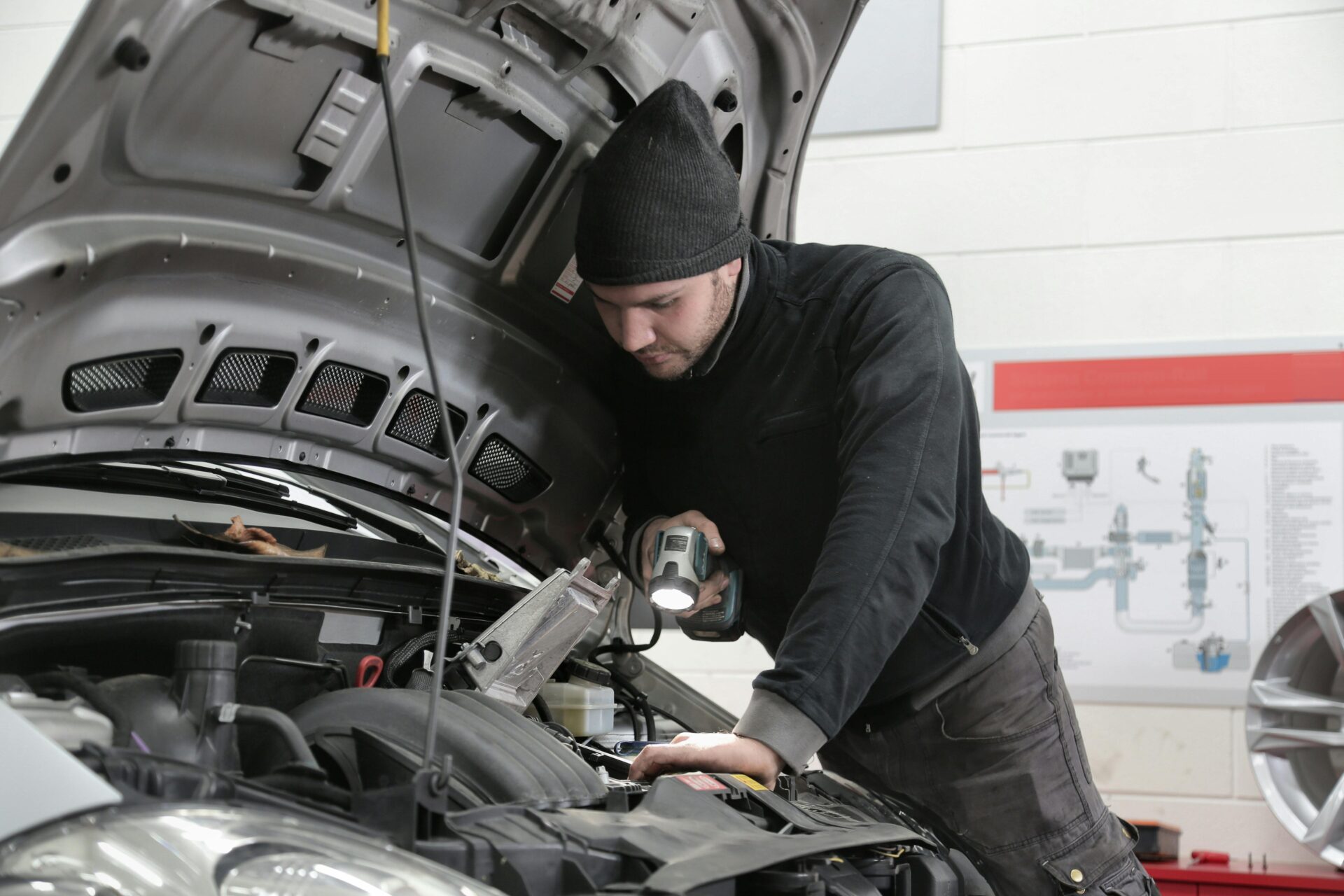 A man wearing a black jacket and a black hat checks a car’s engine.